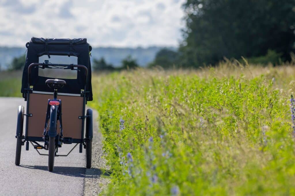 Close-up of a cargo bike with wooden cargo bike box carriers parked on rural road near grassy field on sunny day